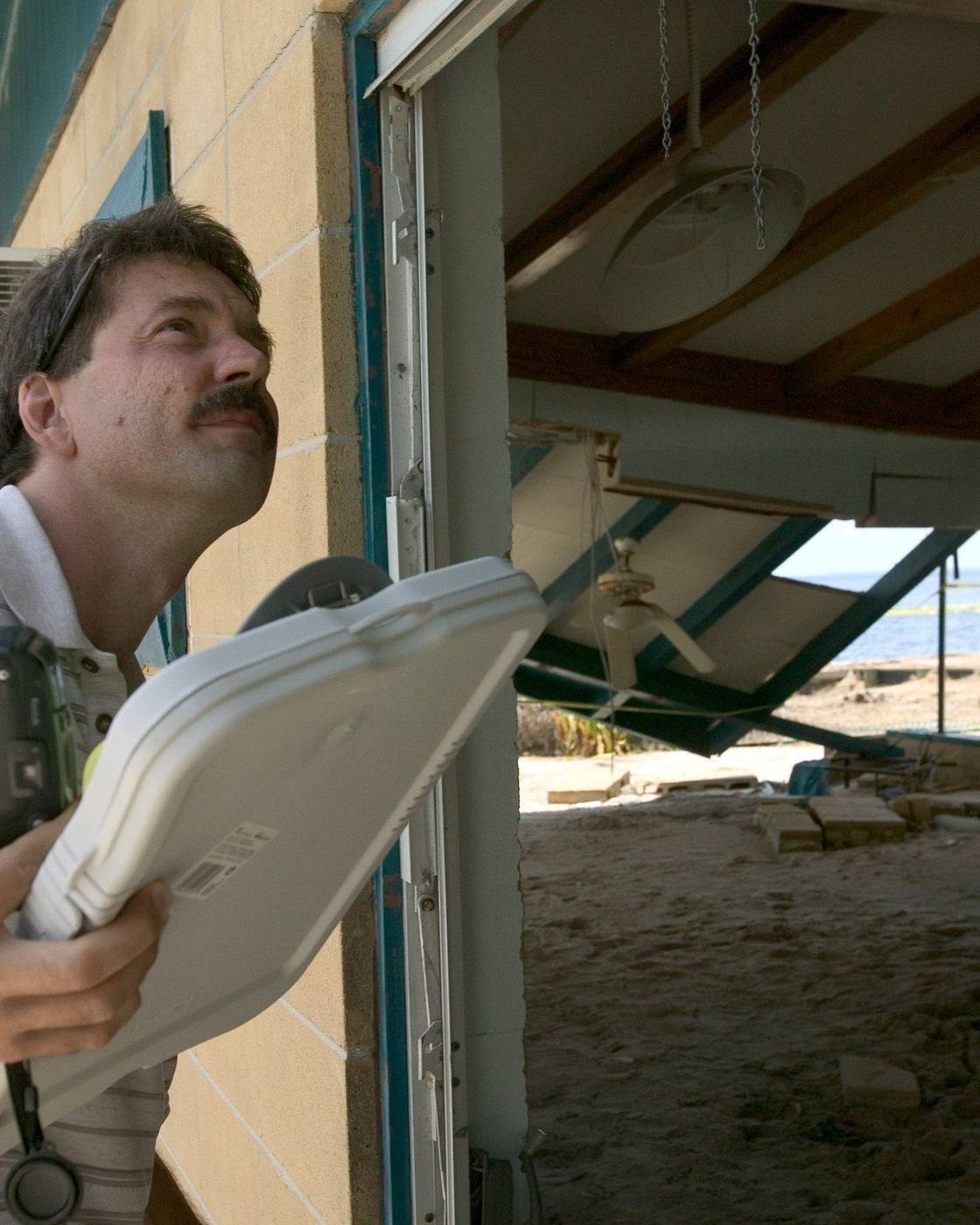 Insurance adjuster with a camera and clipboard looking up at a storm-damaged house