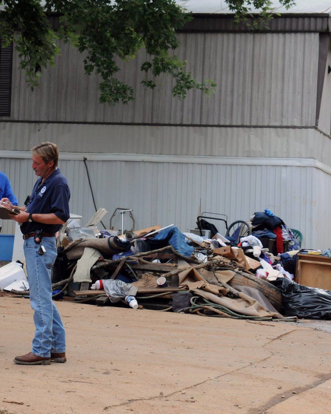 Two assessors comparing notes beside a pile of flood debris
