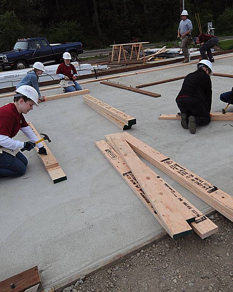 Builders measuring and cutting lumber on a fresh concrete slab