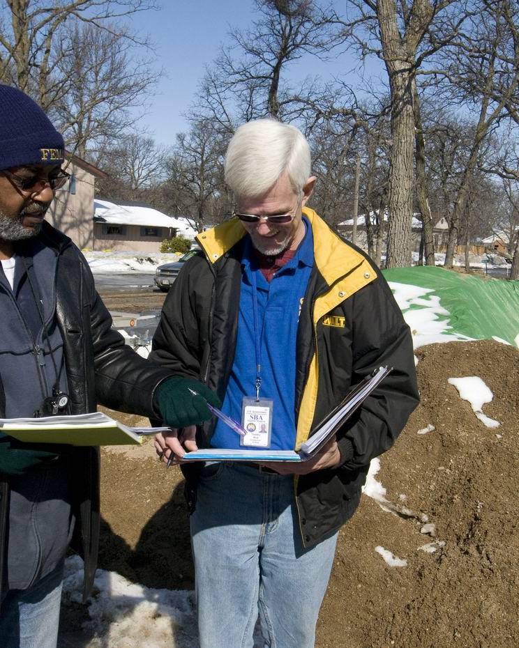 Two damage assessors reviewing notes outside a flood-damaged building