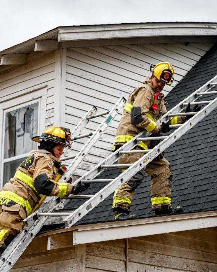 Firefighters climbing a ladder to the roof of a house