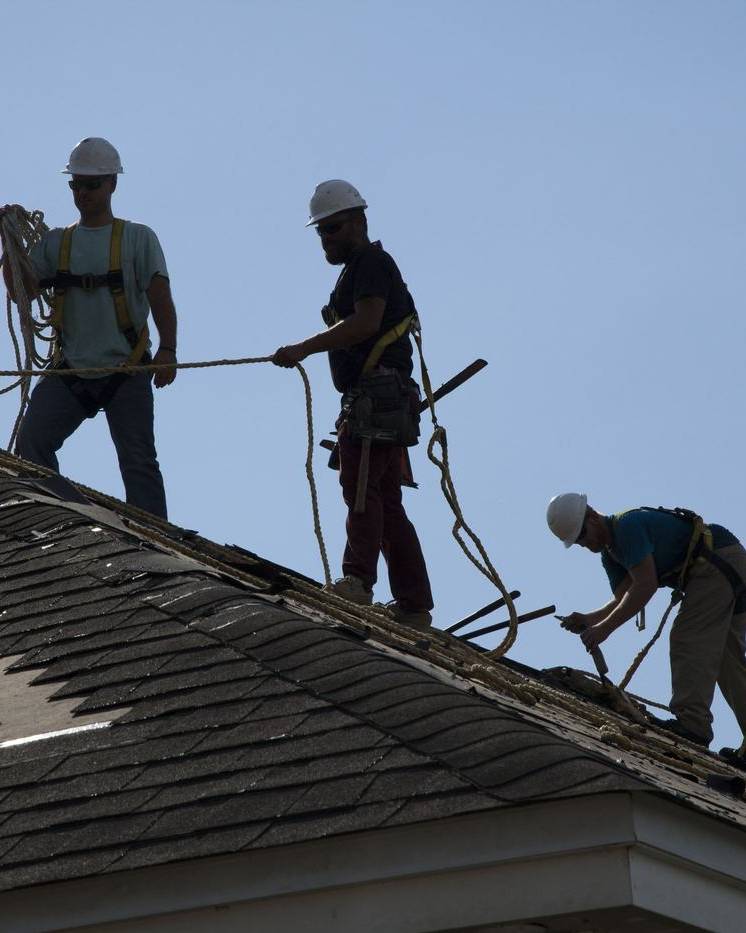 Roofers in hard hats and harnesses working on a house roof