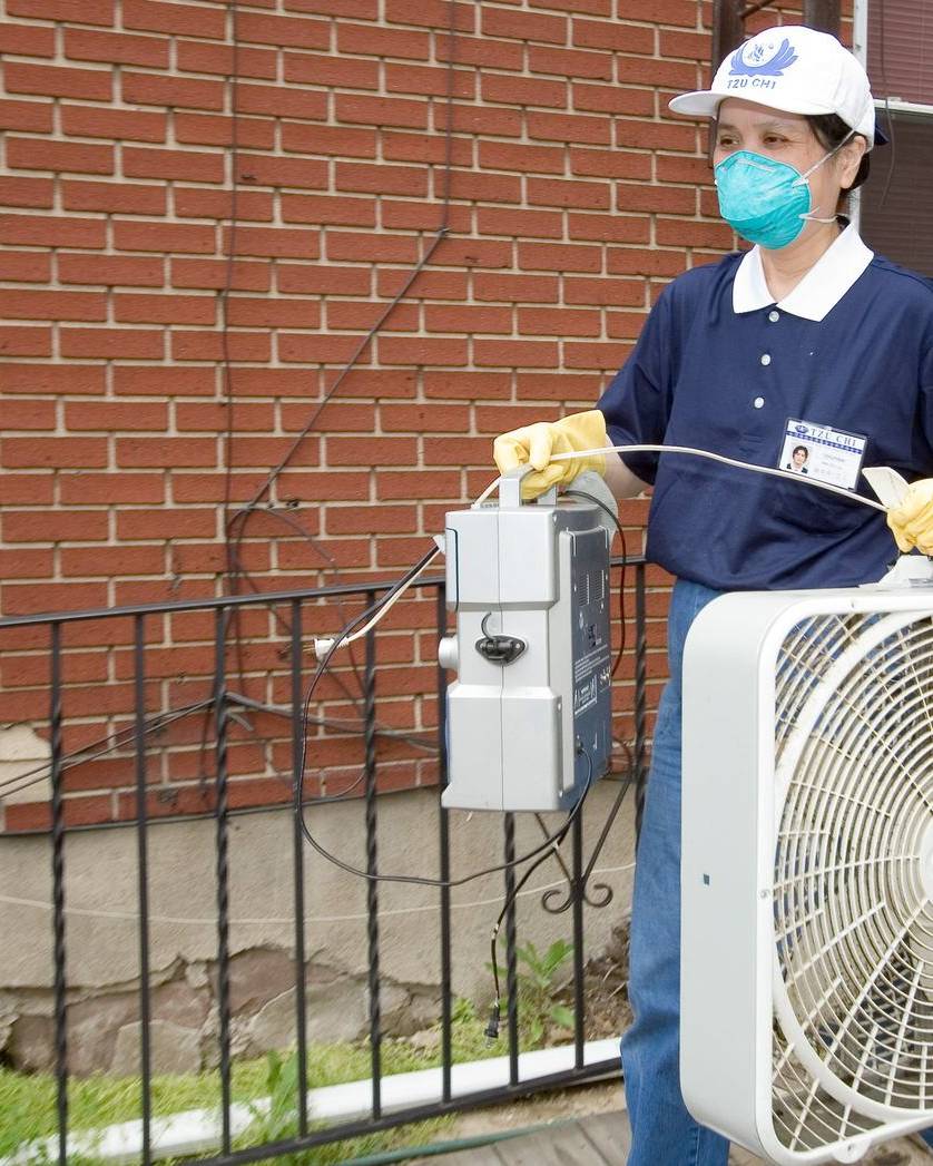 Volunteer in a mask carrying a fan out of a flood-damaged home
