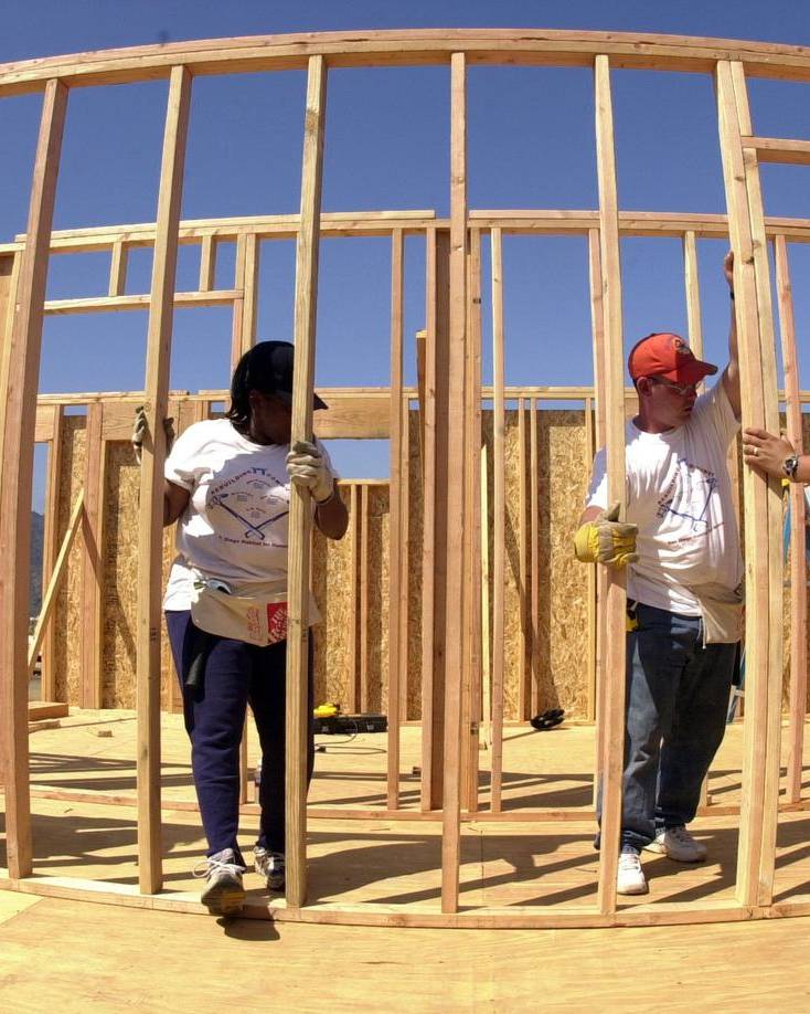 Volunteers in work gloves raising a timber wall frame on a new house