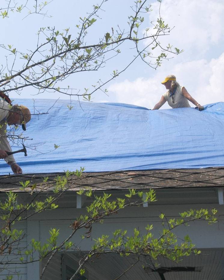 Volunteers laying a blue tarp on a wind-damaged roof