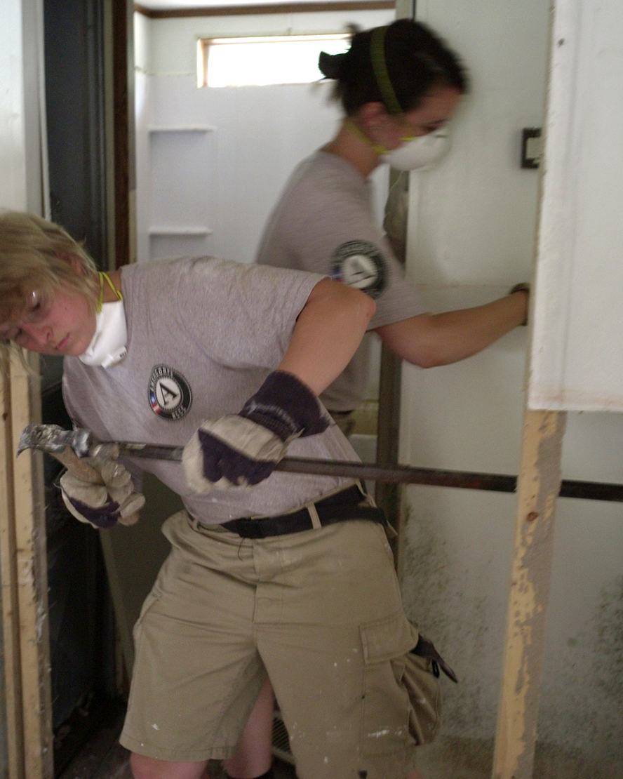 Volunteers in masks tearing out damaged drywall with a wrecking bar