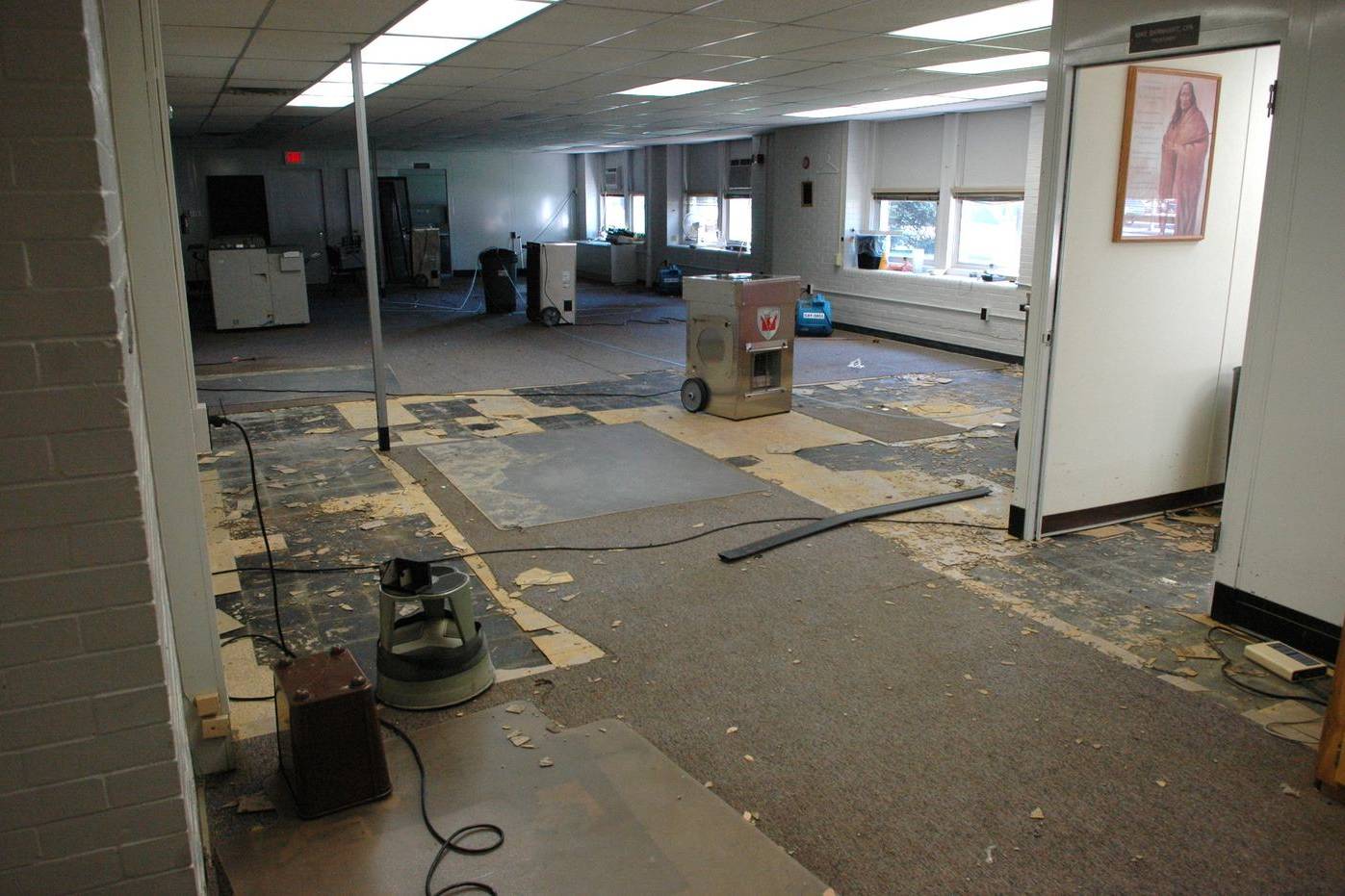 Blowers and dehumidifiers drying wet carpet in a flooded building