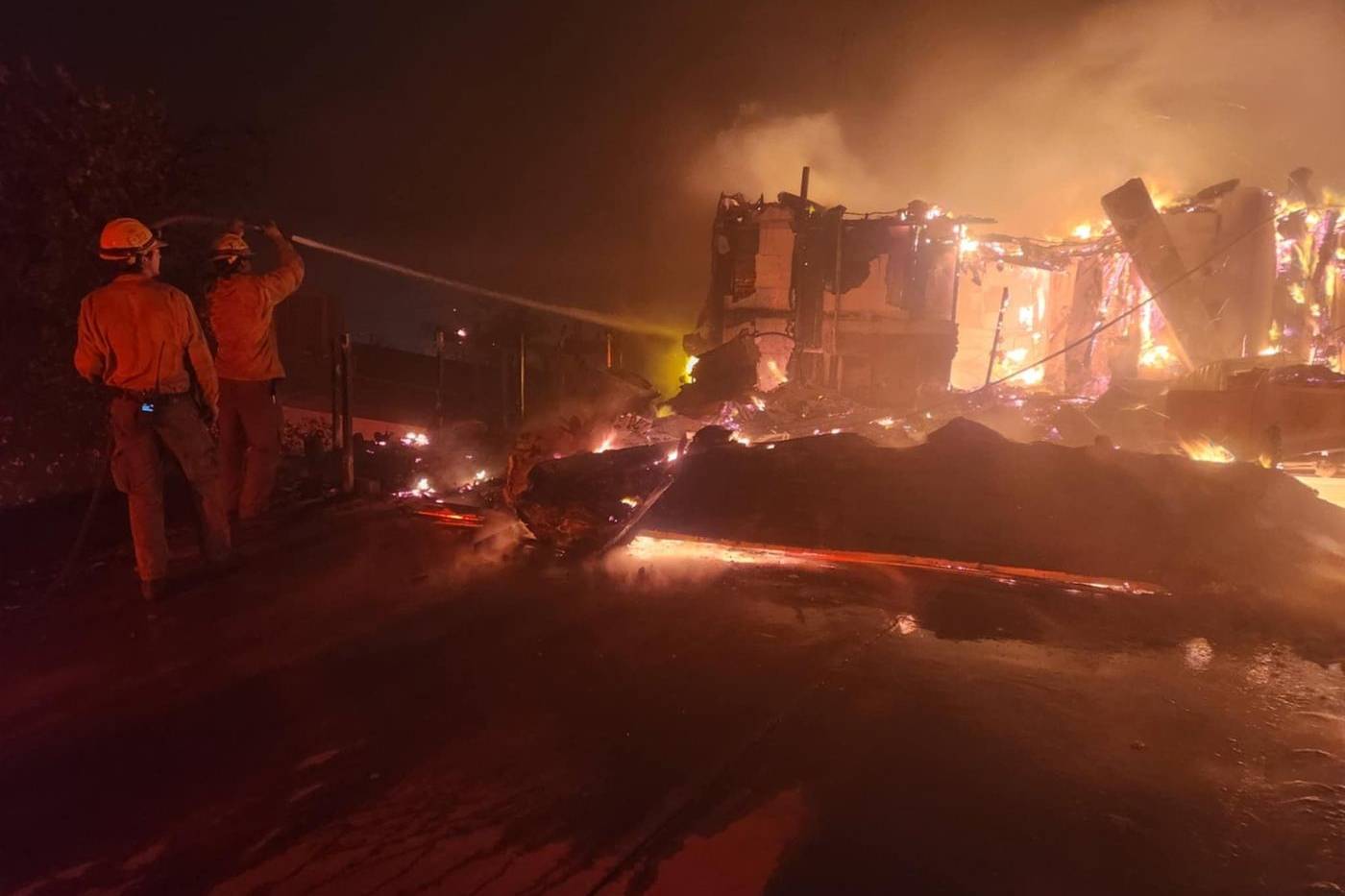 Firefighters spraying a hose on a burning house at night