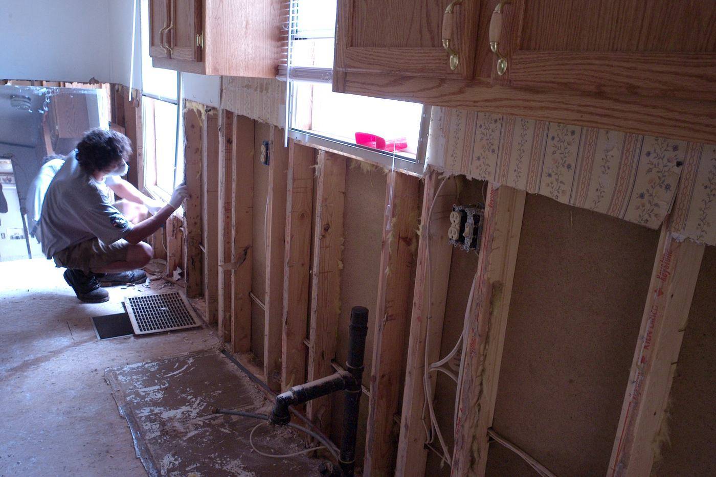 Volunteer removing wet drywall from a flood-damaged kitchen