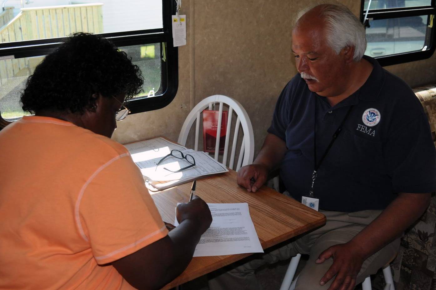 Homeowner signing forms with an official at a kitchen table