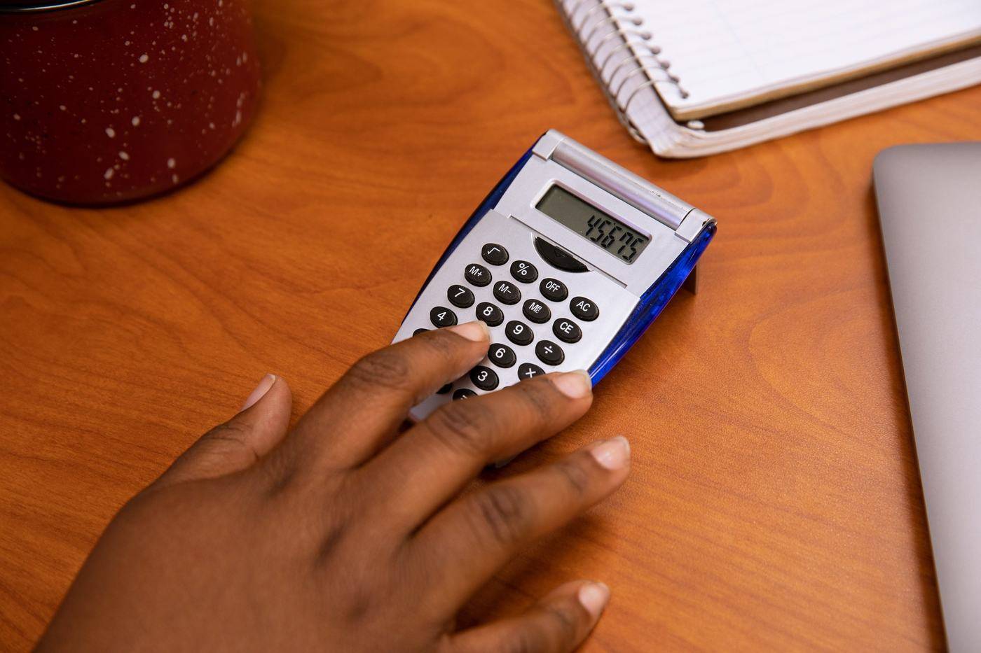Hand using a calculator on a wooden desk